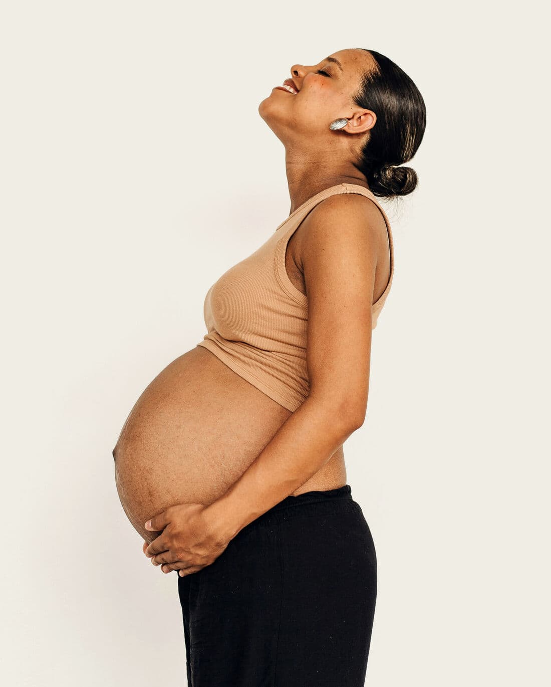 Future maman souriante, de profil, les mains sur son ventre
